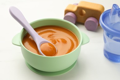 Photo of Bowl and spoon with tasty pureed baby food on white table