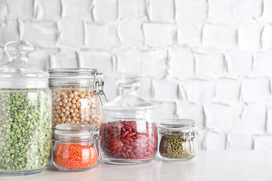 Jars with different cereals on white table against brick wall