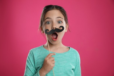 Photo of Cute little girl with fake mustache on pink background