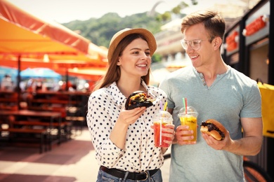 Young happy couple with burgers walking on city street
