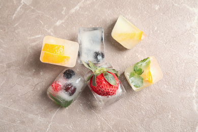 Ice cubes with different berries and mint on grey table, flat lay