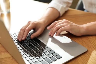 Young woman using laptop for search at wooden table, closeup