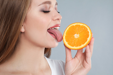 Young woman with cut orange on grey background. Vitamin rich food