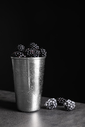 Fresh and frozen blackberries on grey table against dark background