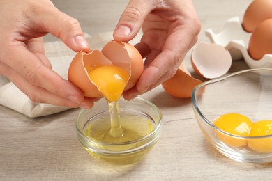 Photo of Woman separating egg yolk from white over glass bowl at wooden table, closeup