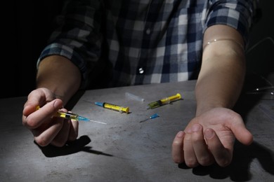 Photo of Drug addiction. Man with syringe at grey table, closeup
