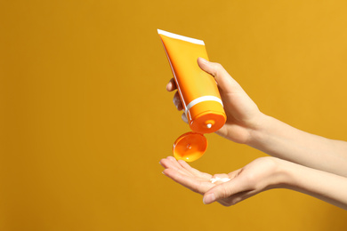 Woman applying sun protection cream on hand against yellow background, closeup. Space for text