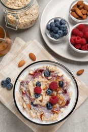 Photo of Tasty oatmeal porridge with toppings served on grey table, flat lay