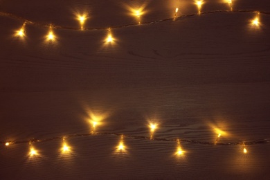 Frame of beautiful glowing Christmas lights on wooden table, top view. Space for text
