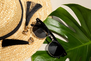 Stylish sunglasses, tropical leaf, earrings and straw hat on sand, flat lay