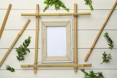 Flat lay composition with bamboo frame and green leaves on white wooden table