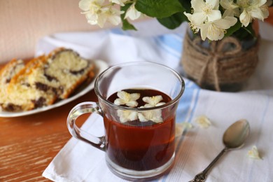 Glass cup of aromatic tea, tasty dessert and beautiful jasmine flowers on wooden table
