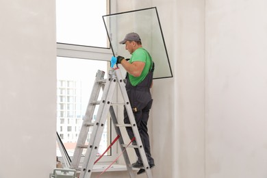 Worker in uniform installing double glazing window indoors