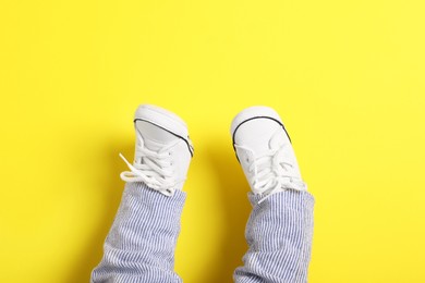 Photo of Little baby in stylish gumshoes on yellow background, top view. Space for text
