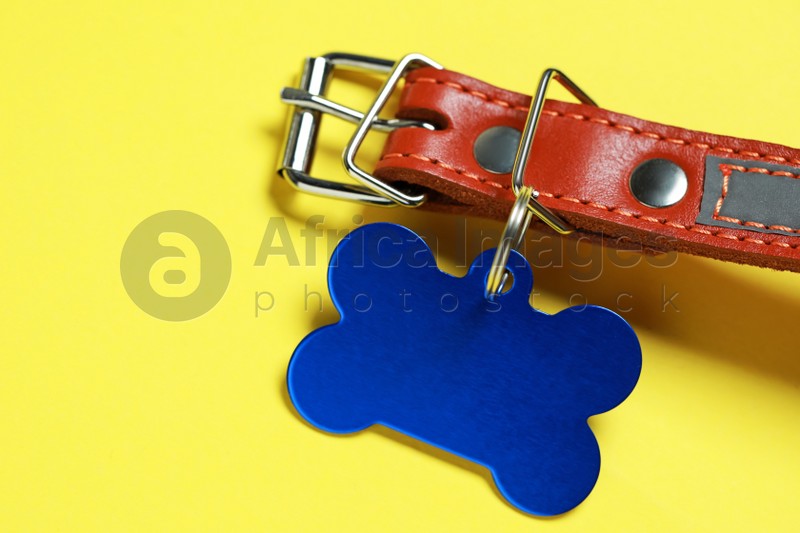 Leather dog collar with blue tag in shape of bone on yellow background, closeup. Space for text