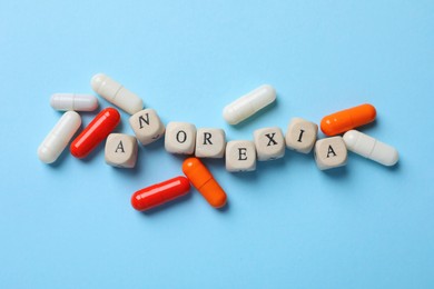 Word Anorexia of wooden cubes and pills on light blue background, flat lay
