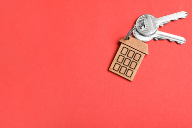 Keys with trinket in shape of house on red background, top view and space for text. Real estate agent services