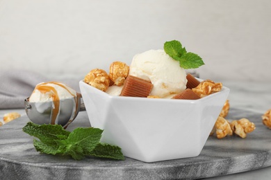 Bowl of delicious ice cream with caramel candies, popcorn and mint on table
