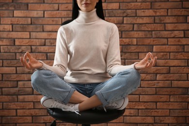 Woman meditating on chair near brick wall, closeup
