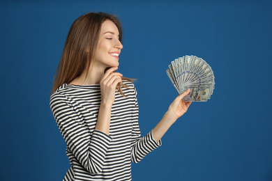 Happy young woman with cash money on blue background