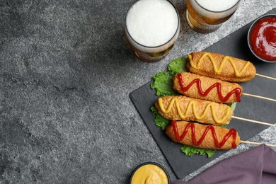 Delicious deep fried corn dogs with lettuce and sauces on grey table, flat lay. Space for text