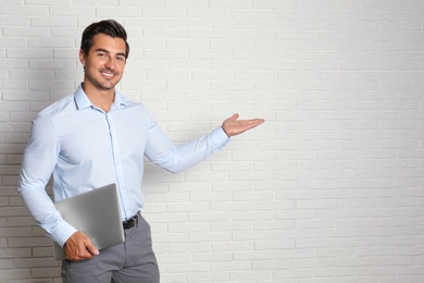 Young male teacher with laptop near brick wall. Space for text