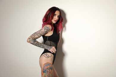 Beautiful woman with tattoos on body against light background. Space for text