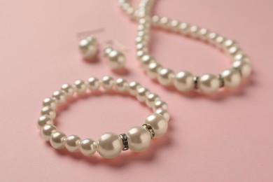 Elegant necklace, bracelet and earrings with pearls on pink background, closeup