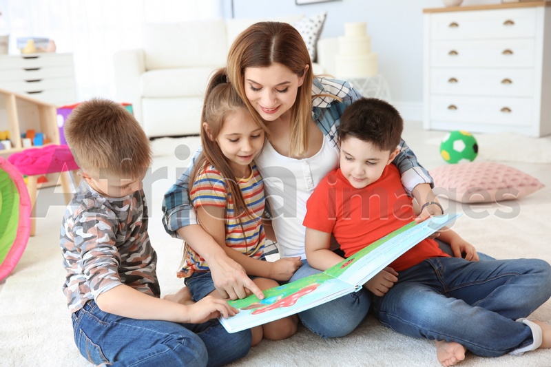 Cute little children reading book on floor with young mother in playing room