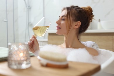 Beautiful woman with glass of wine enjoying bubble bath at home