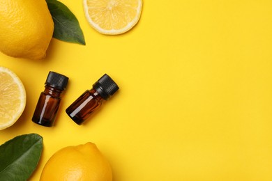 Bottles of citrus essential oil, fresh lemons and leaves on yellow background, flat lay. Space for text