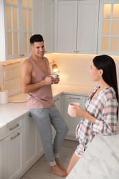 Photo of Happy couple wearing pyjamas with cups of coffee in kitchen
