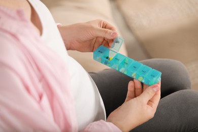 Pregnant woman holding box with pills on blurred background, closeup
