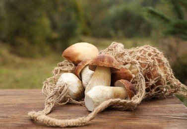 String bag and fresh wild mushrooms on wooden table outdoors, closeup