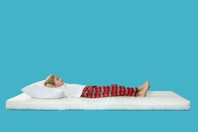 Photo of Little girl lying on comfortable mattress against light blue background, space for text