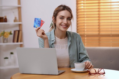 Woman with credit cards using laptop for online shopping at wooden table indoors