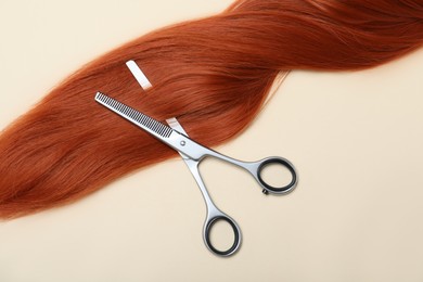 Professional hairdresser scissors and hair strand on beige background, flat lay. Haircut tool