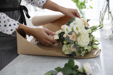 Florist wrapping beautiful wedding bouquet with paper at light grey marble table, closeup