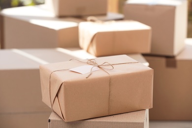 Parcel with tag and blurred stacked boxes on background, indoors