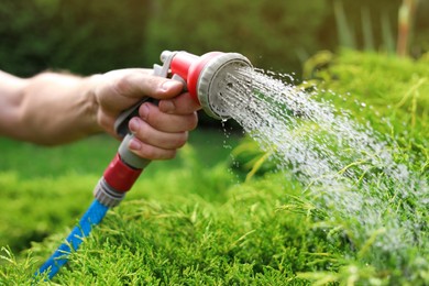 Man watering green grass from hose in garden, closeup