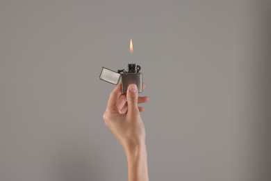 Woman holding lighter with burning flame on grey background, closeup