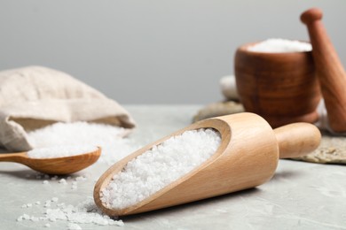 Natural sea salt in wooden scoop on light grey marble table, closeup