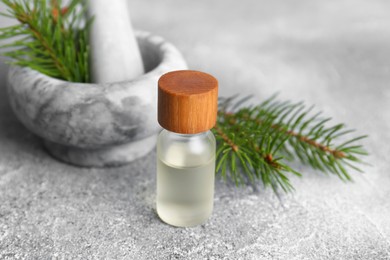 Bottle of aromatic essential oil and mortar with pine branch on light grey table, closeup