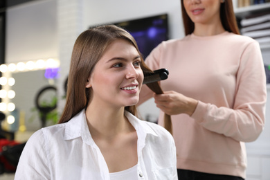 Hairdresser using straightener to style client's hair in salon