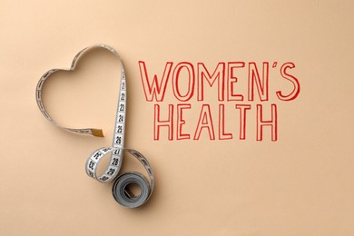 Measuring tape near words Women's Health on beige background, top view