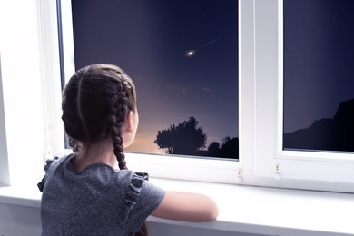 Image of Cute little girl near window and looking at shooting star in beautiful night sky
