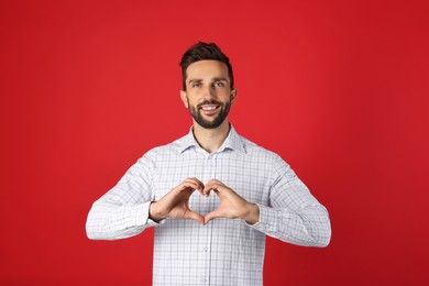 Happy man making heart with hands on red background