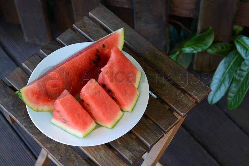 White plate with sliced watermelon on wooden stool outdoors. Space for text