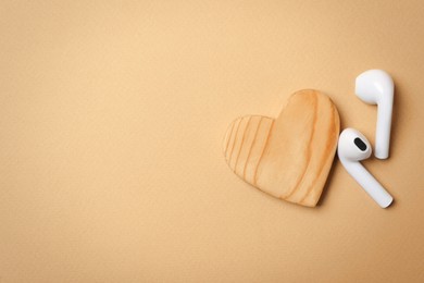 Modern earphones and heart on beige background, flat lay with space for text. Listening love music songs