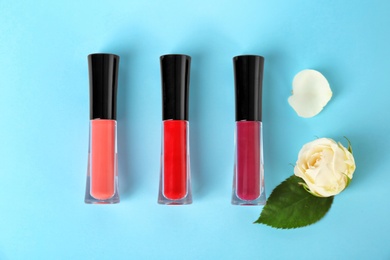Lip glosses and flowers on color background
